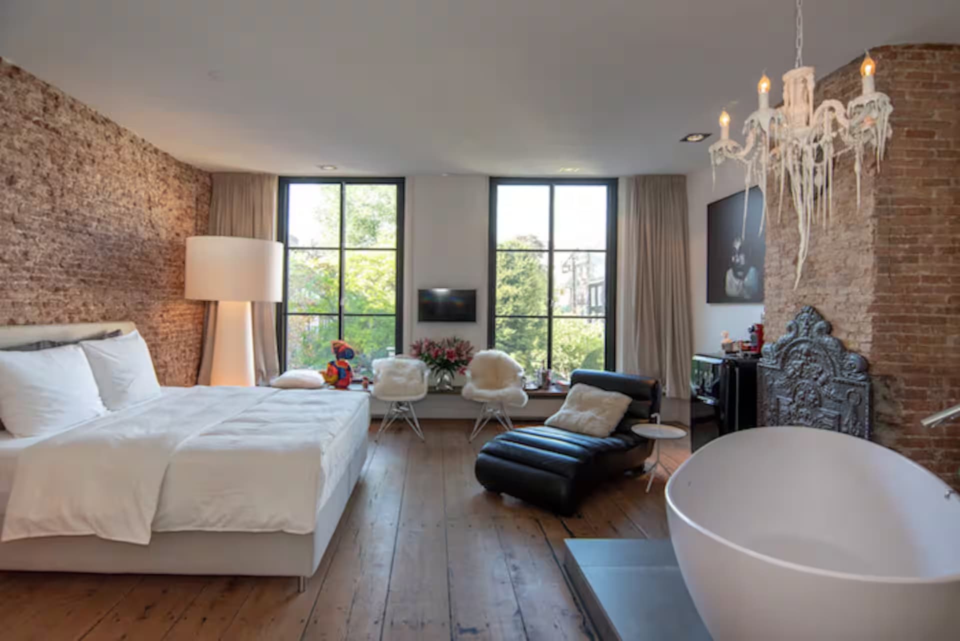 Love Suite Wolvenstraat 16 — kingsize bed tegen brick-wall met kroonluchter, vrijstaand bad en zithoek bij grachten-ramen