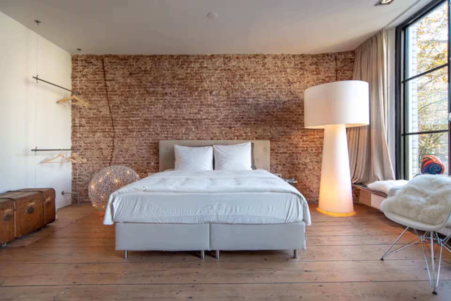 Love Suite — bed tegen brick-wall met witte tafellamp, kledingrek en raam aan zijkant