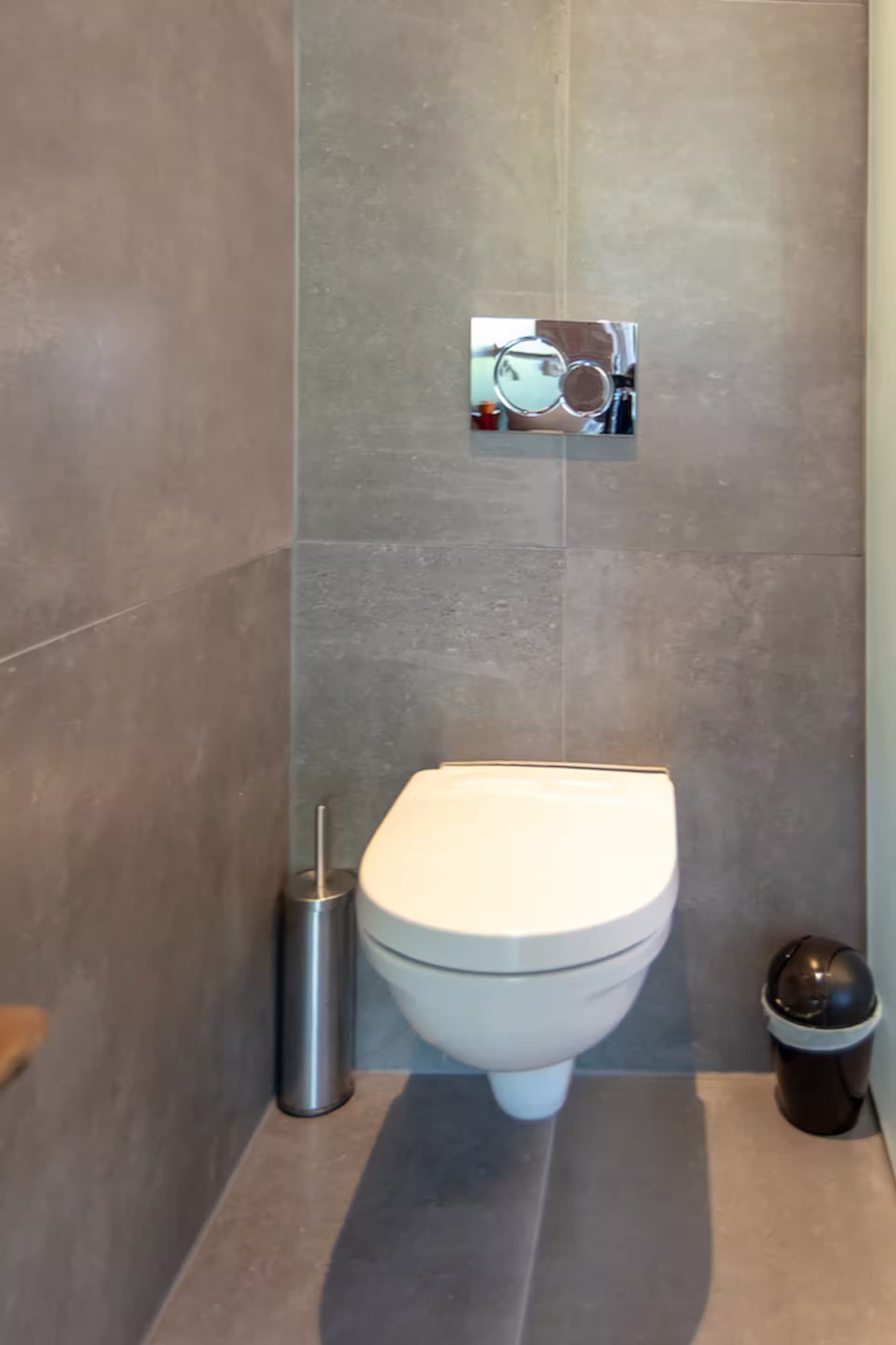 Love Suite — toilet-detail met grijze tegels en chromen drukknop